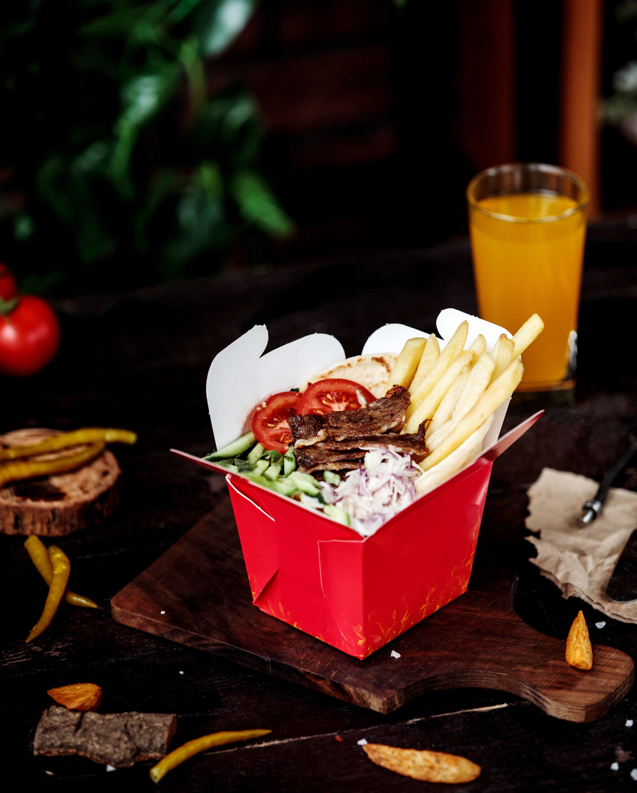 side view of kebab meat with vegetable salad and french fries in a cardboard bag on a wooden cutting board